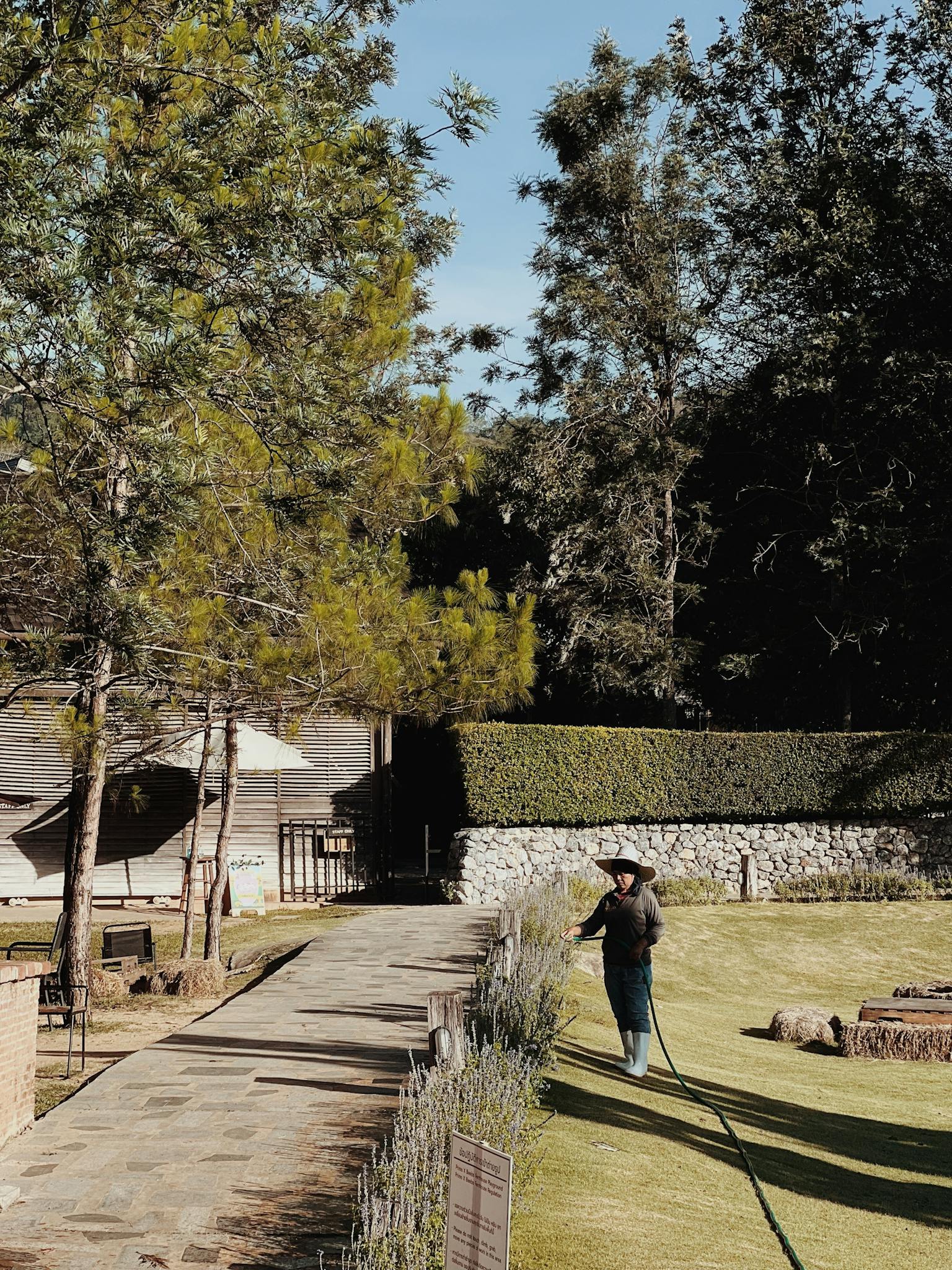 A gardener waters the lawn in a beautifully landscaped outdoor park under clear skies.