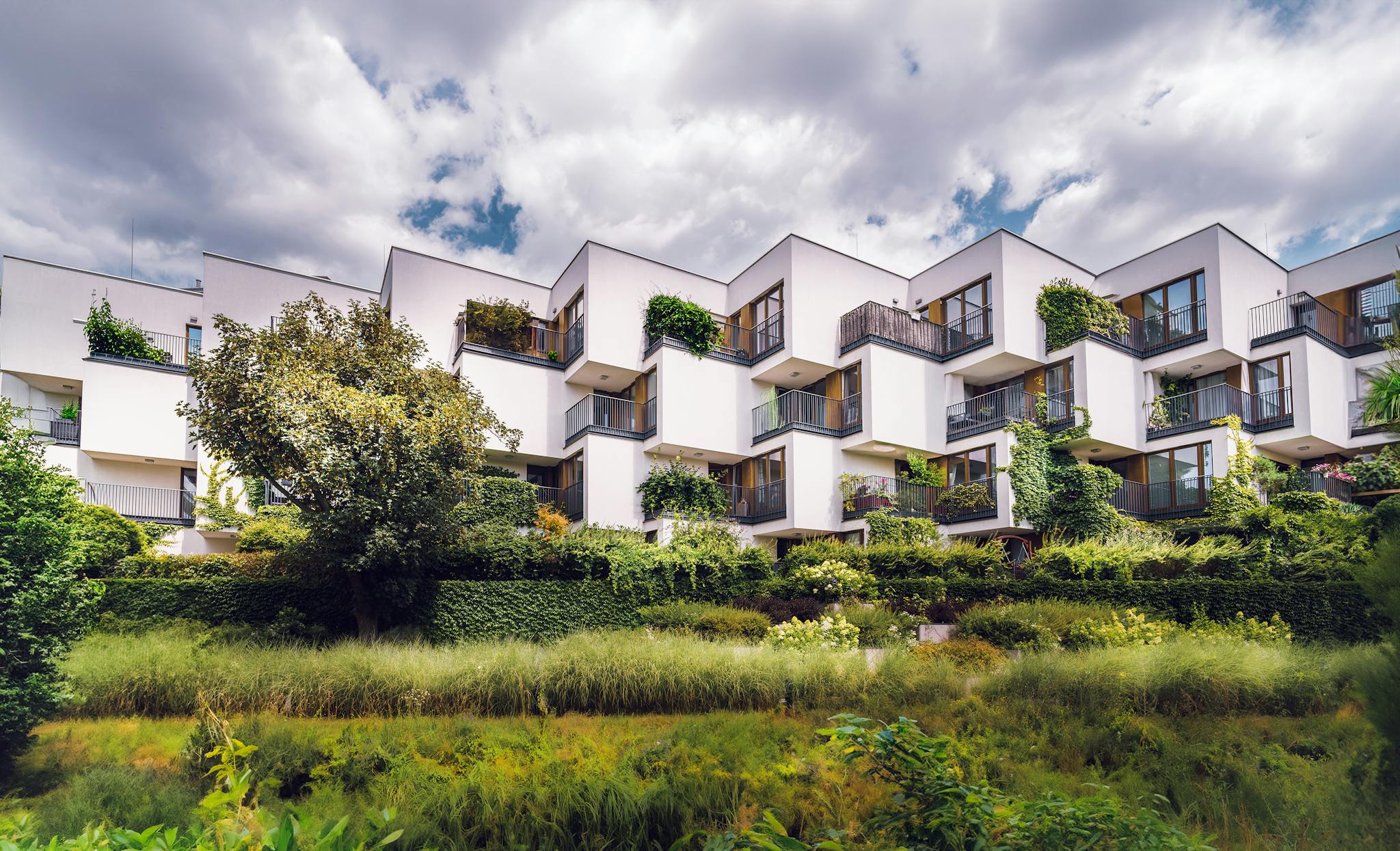 Contemporary apartment complex featuring sustainable architecture with lush greenery and open balconies.